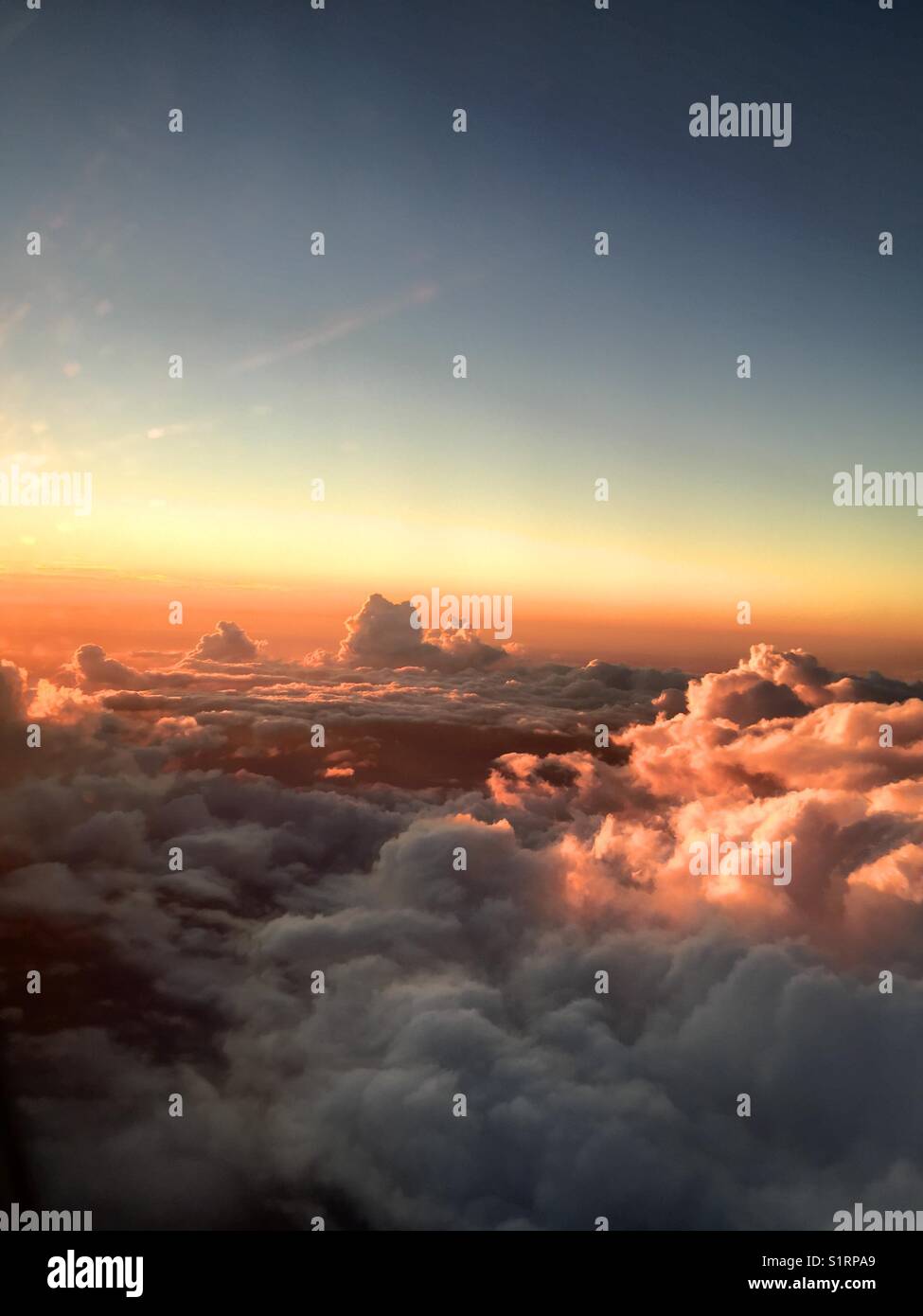 Colourful clouds in sunset sky shot from an airplane. View over the clouds and blue sky . Shot above the clouds through a airplane window - Smartphone Captured Stock Image