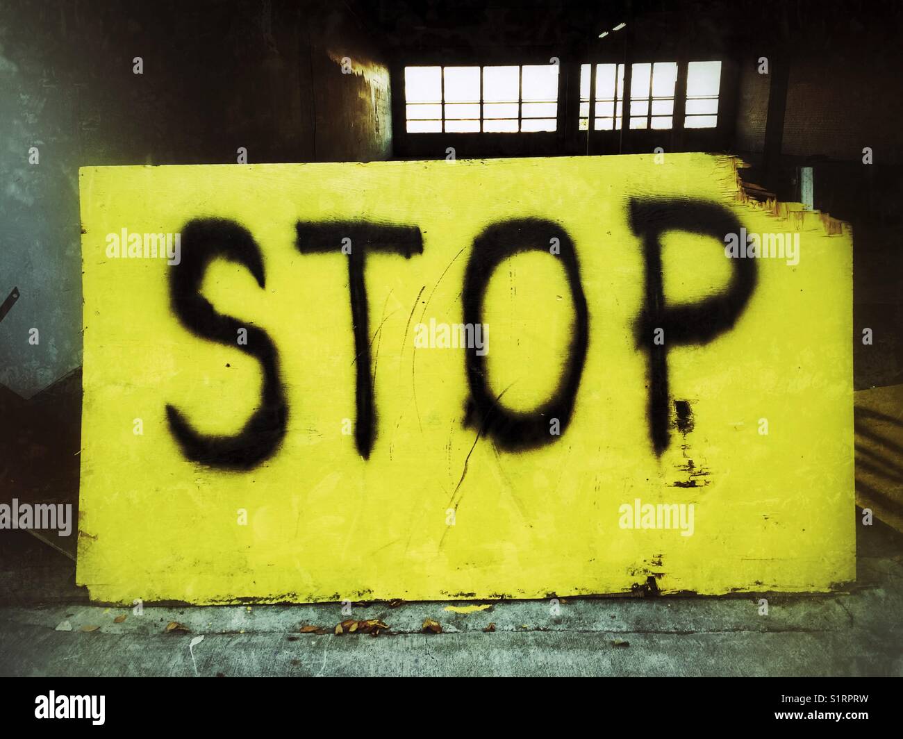 Spray painted black word stop on an old yellow board sign at the entrance to abandoned garage Stock Photo