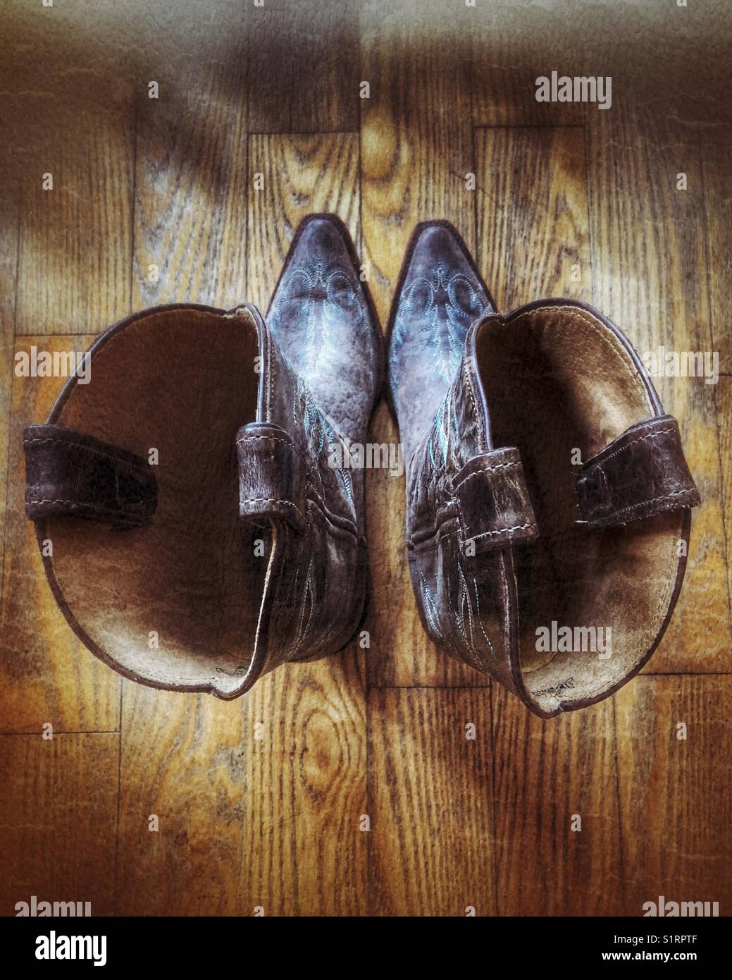 Looking down into an old pair of cowgirl boots on a wooden floor Stock Photo