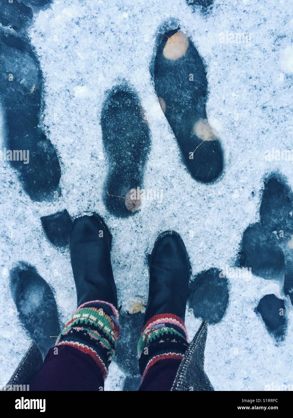 Boots and knitted leg warmers standing on the sidewalk with first snow