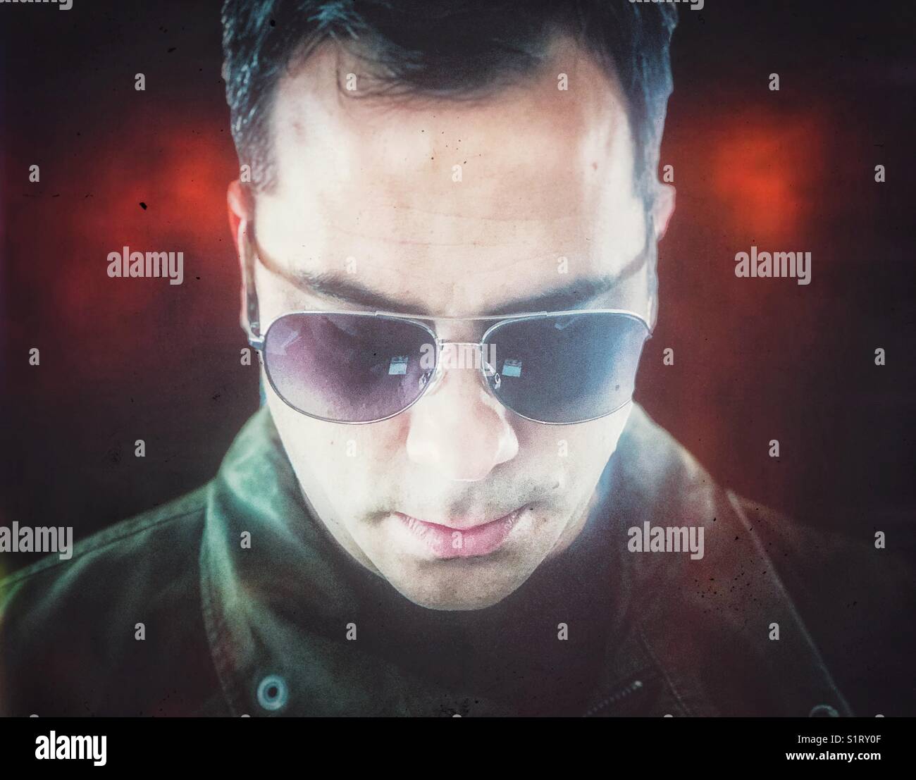 Dark haired man wearing aviator sunglasses looking down at smartphone - Smartphone Captured Stock Image