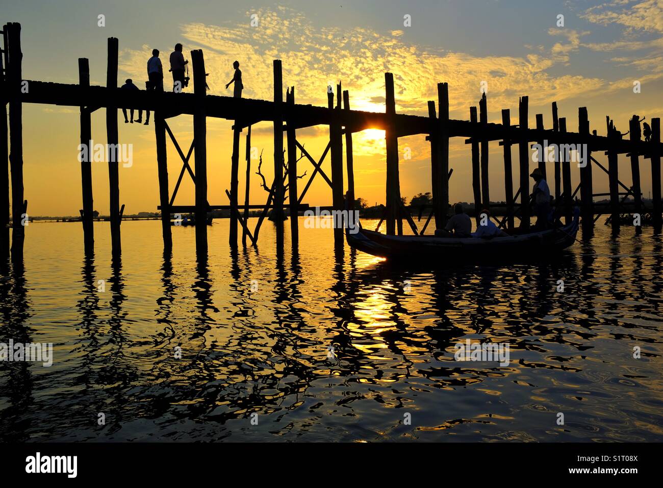 Boat crossing in front of U Bein Bridge in Mandalay, Myanmar at sunset - Smartphone Captured Stock Image