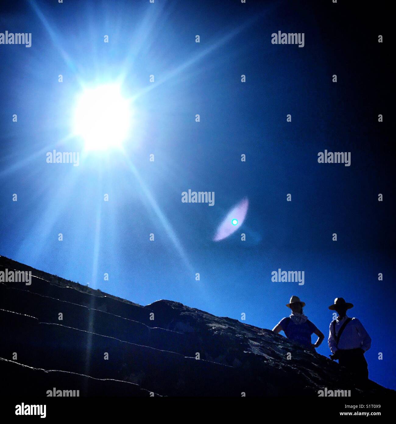 A couple of tourists wearing hats in the pyramid of the sun in Teotihuacan, Mexico City, Mexico. The lens of the phone creates an eye. - Smartphone Captured Stock Image