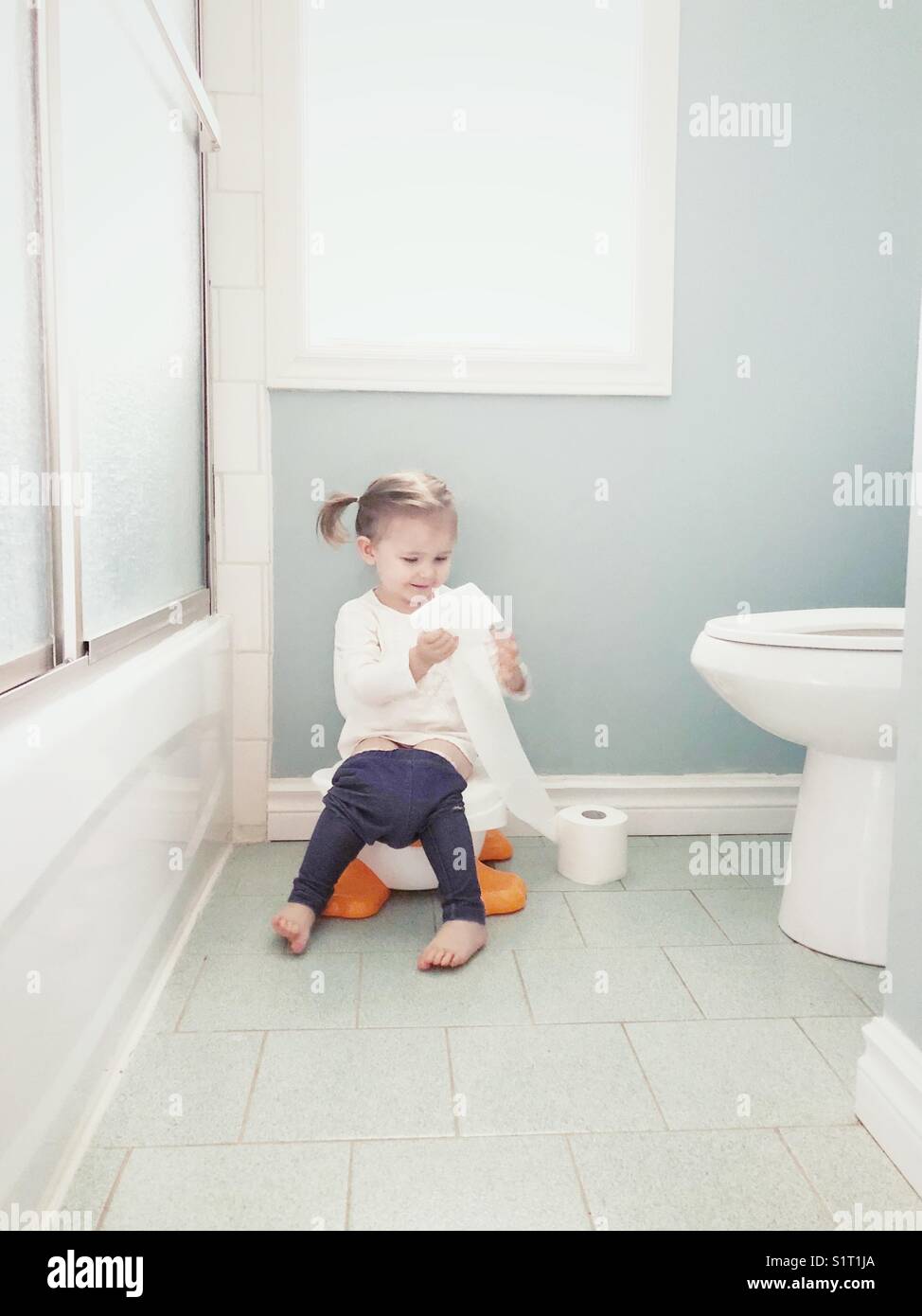 Potty training 2 year old toddler girl sitting on potty playing with toilet  paper roll Stock Photo - Alamy