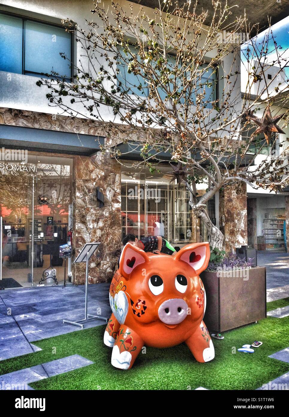 Child climbing on an orange good luck pig. - Smartphone Captured Stock Image