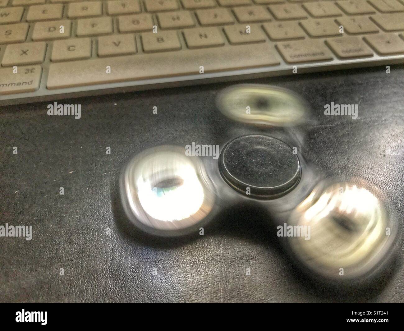 Fidget spinner, spinning on a leather topped office desk with a computer keyboard behind. - Smartphone Captured Stock Image