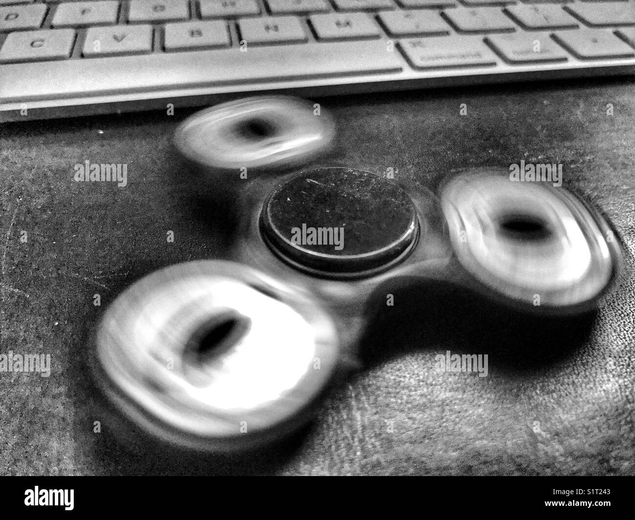 Fidget spinner, spinning on a leather topped office desk with a computer keyboard behind. - Smartphone Captured Stock Image