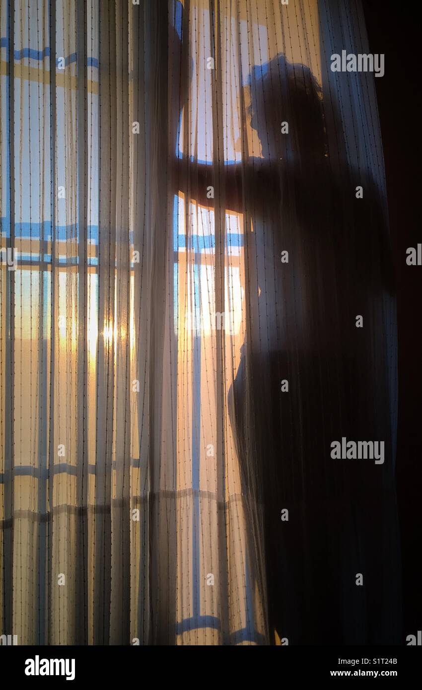 Silhouette of woman looking out of window at sunset - Smartphone Captured Stock Image