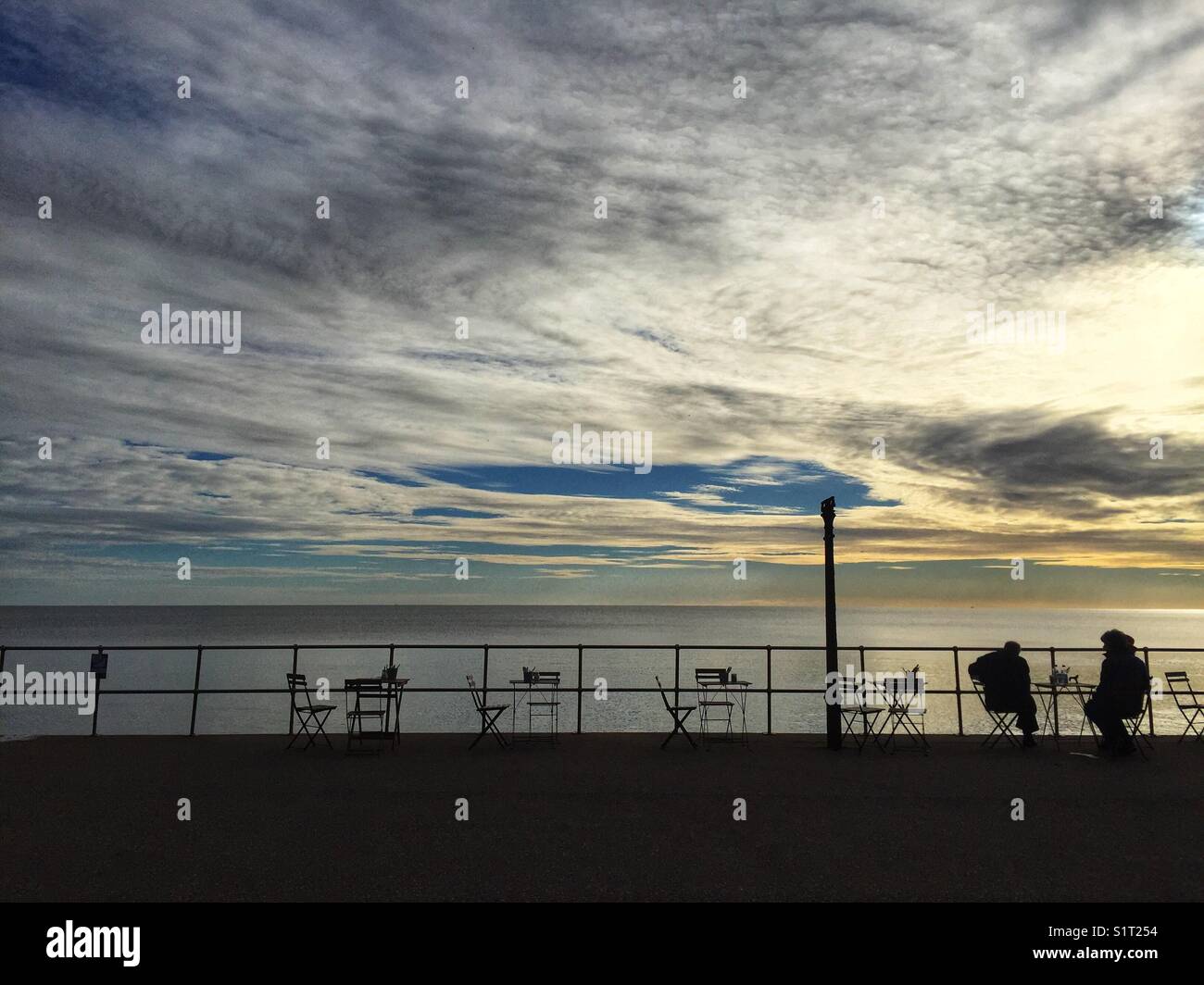People sit along the Promenade at Seaton beach in Devon, England on November 13 2017 - Smartphone Captured Stock Image