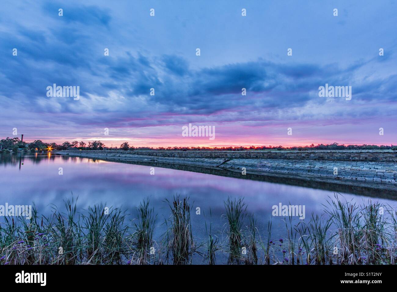 Colourful sunrise reflected in lake and stone wall - Smartphone Captured Stock Image