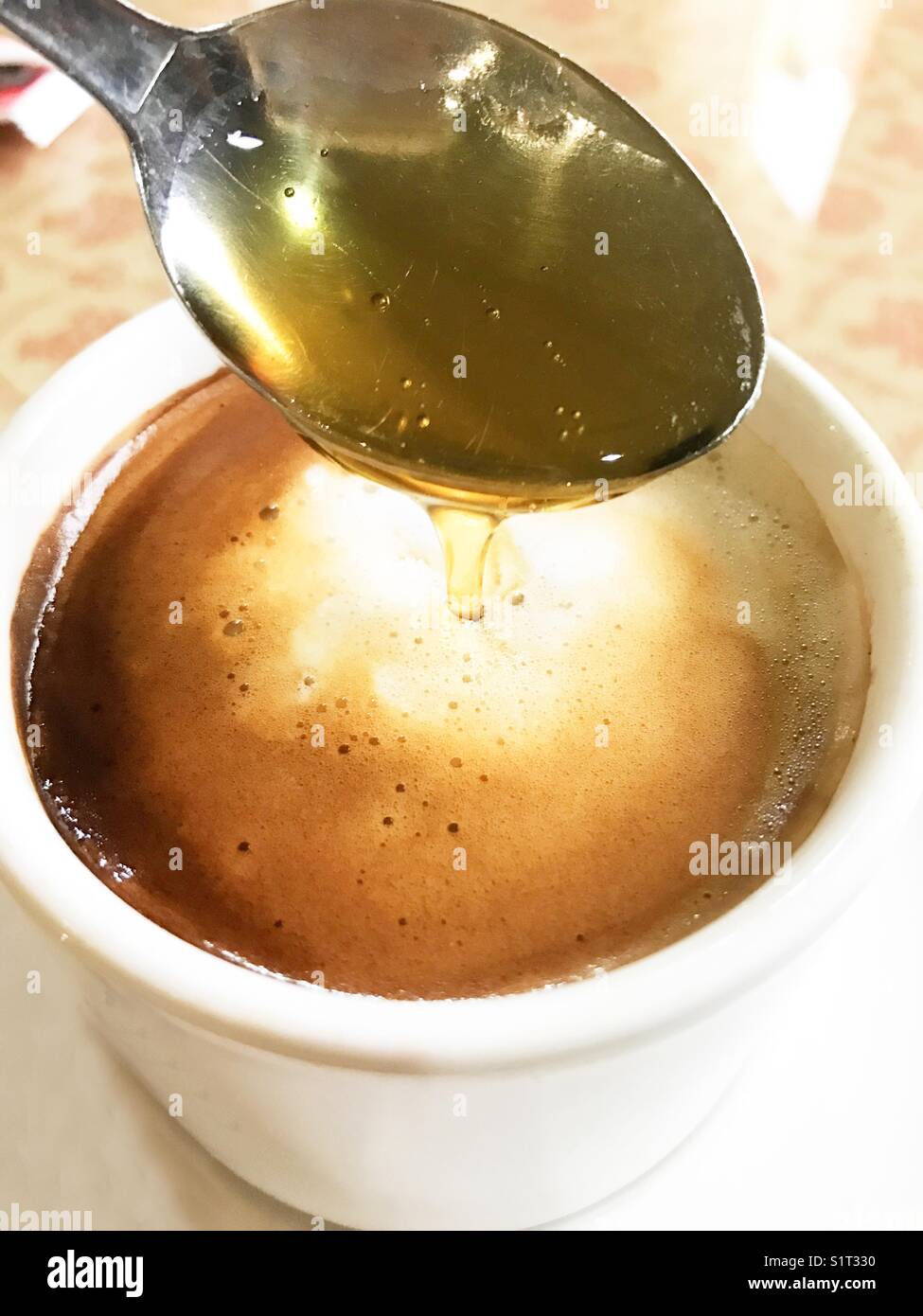 Spoon pouring honey in a cup of coffee. - Smartphone Captured Stock Image