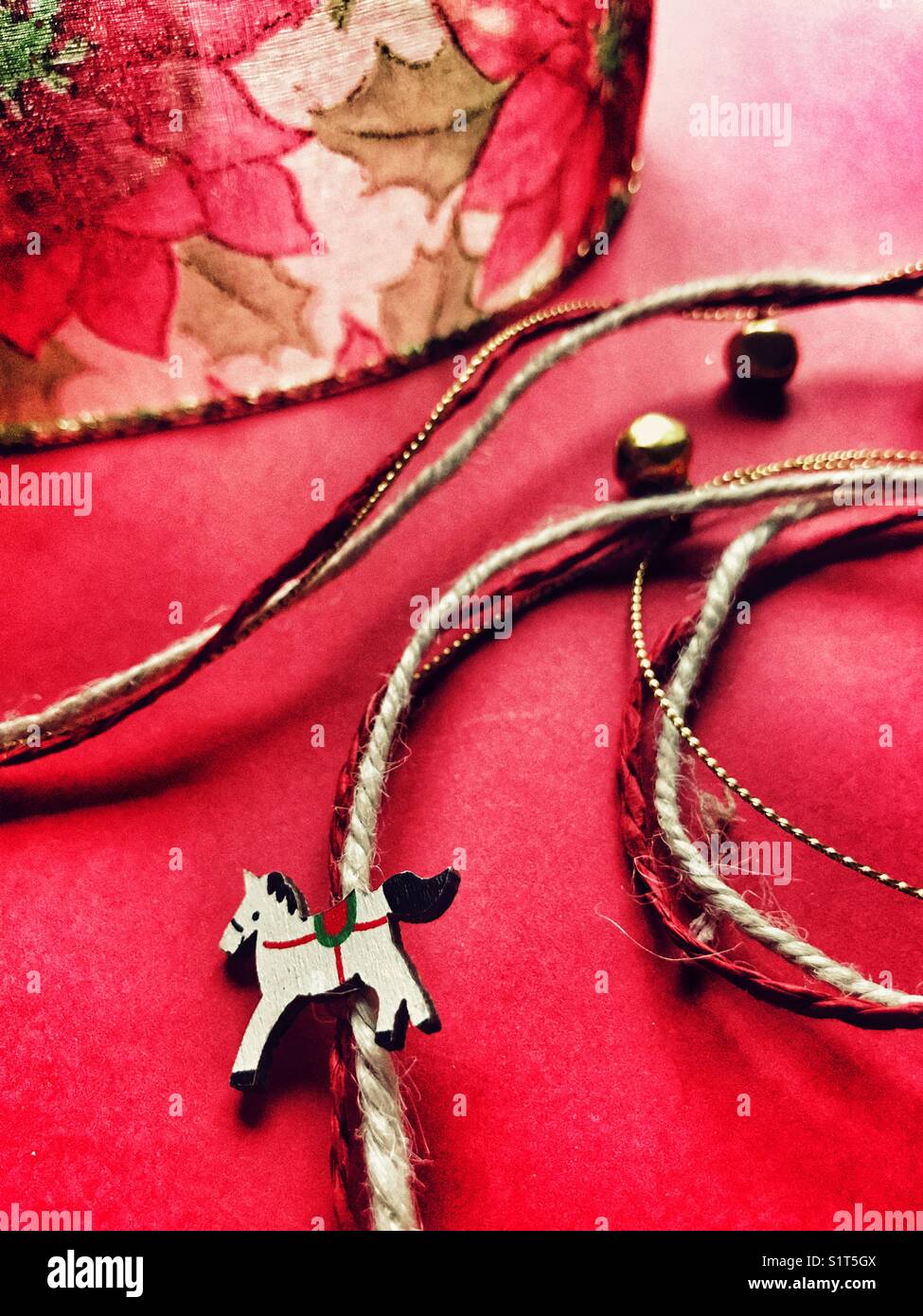 Christmas ribbon, made up of strands of ribbon and string with bells and rocking horses, with poinsettia wire ribbon behind - Smartphone Captured Stock Image