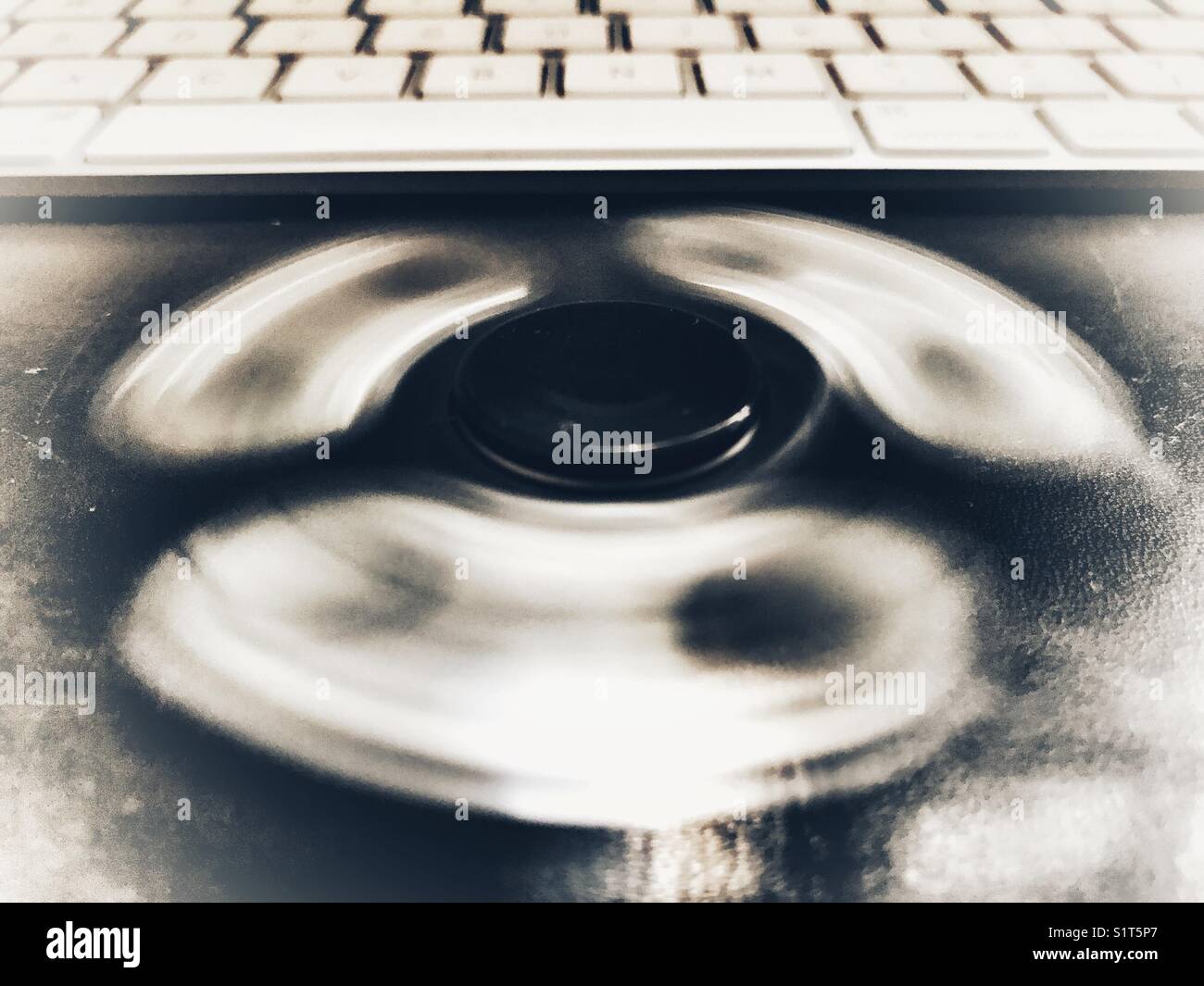 Fidget spinner. spinning on a leather topped desk in front of a computer keyboard. - Smartphone Captured Stock Image