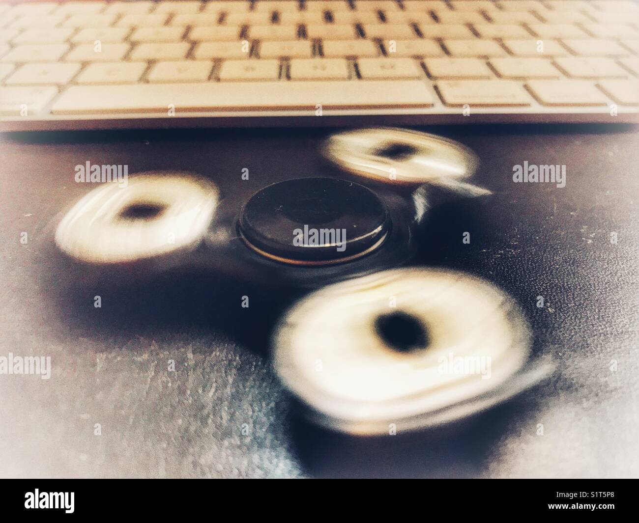 Fidget spinner. spinning on a leather topped desk in front of a computer keyboard. - Smartphone Captured Stock Image