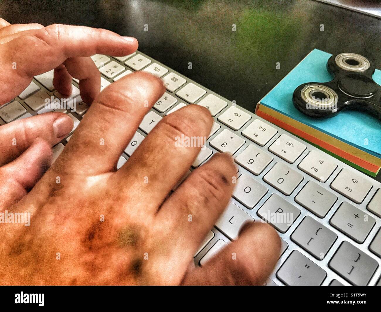 POV personal perspective, Millennial woman’s hands on computer keyboard with a fidget spinner on a blue notepad. - Smartphone Captured Stock Image
