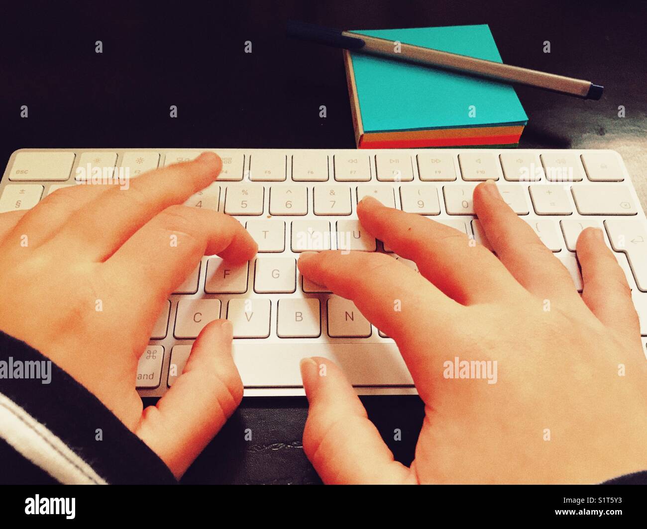Millennial woman’s hands on computer keyboard with a pen on a blue notepad. - Smartphone Captured Stock Image