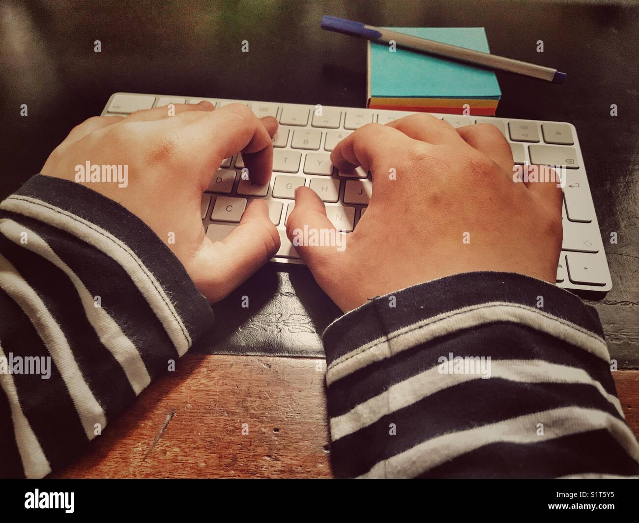 Millennial woman’s hands on computer keyboard with a pen on a blue notepad. - Smartphone Captured Stock Image