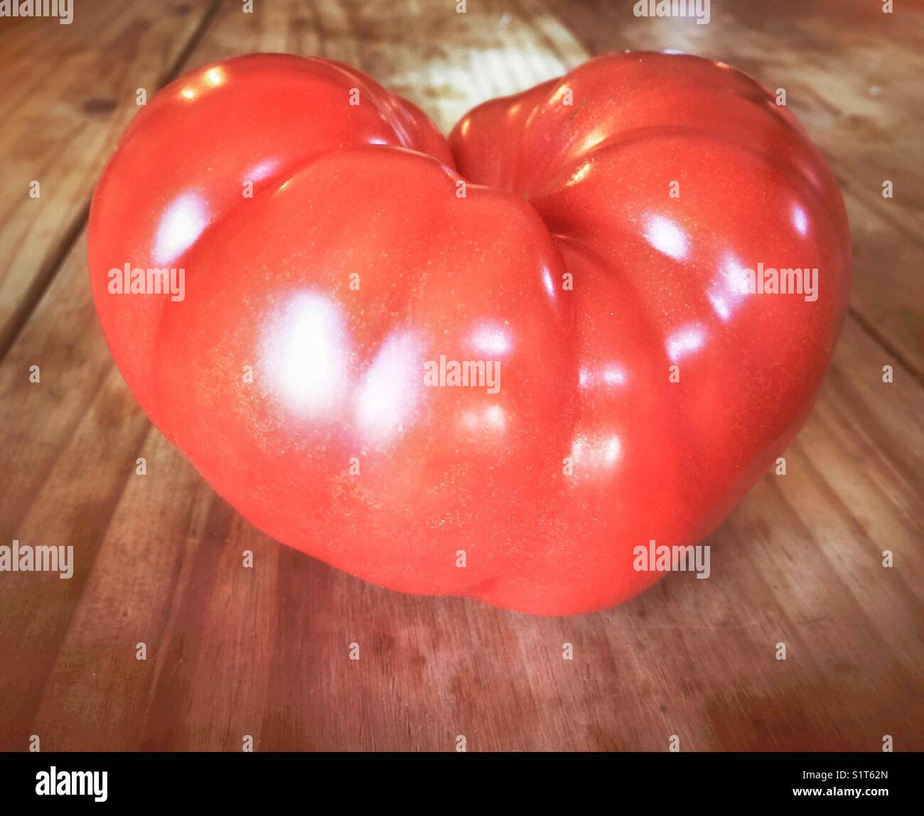 Giant beefsteak tomato shaped like a heart on a wooden table - Smartphone Captured Stock Image