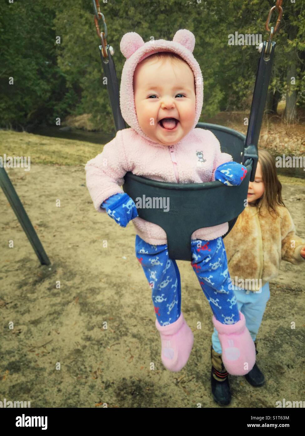 Baby girl being pushed in an infant swing by her older sister at a park