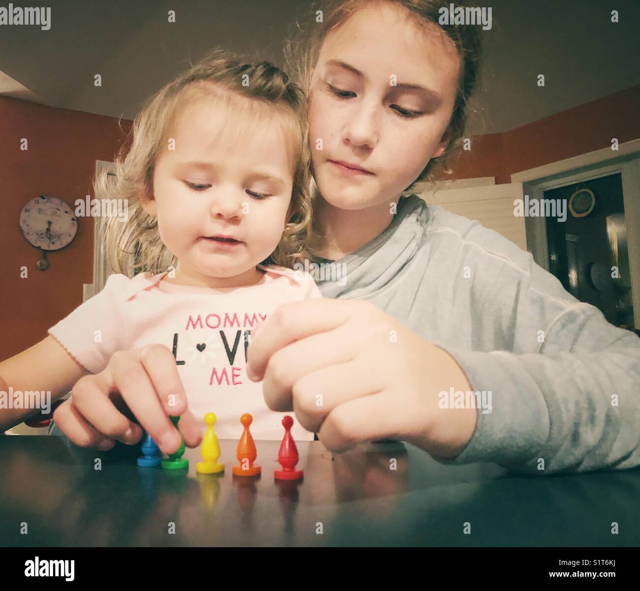 Big sister teaching baby sister colours using game pieces - Smartphone Captured Stock Image