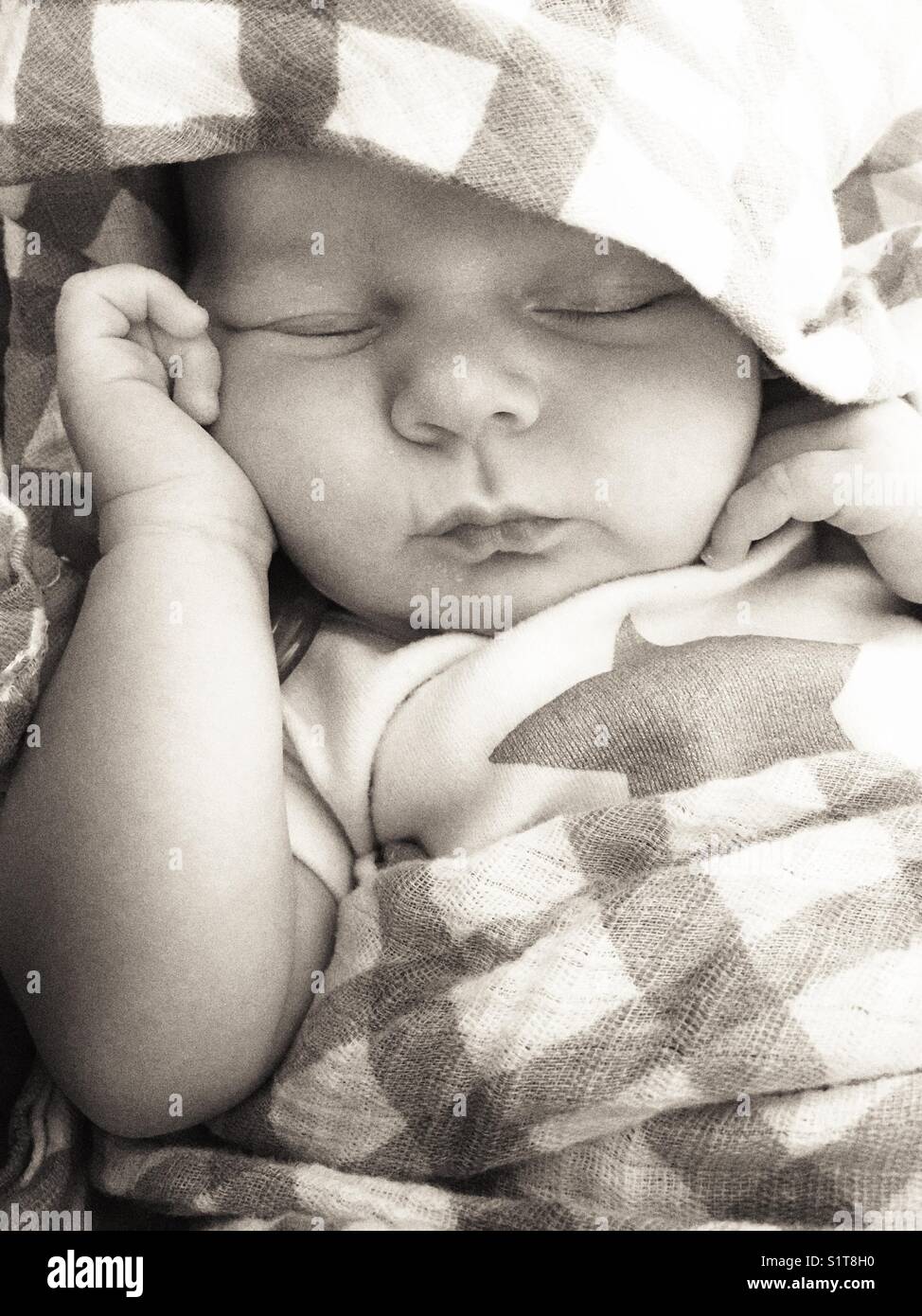 Black and white image of newborn baby sleeping in a plaid pattern swaddle blanket - Smartphone Captured Stock Image