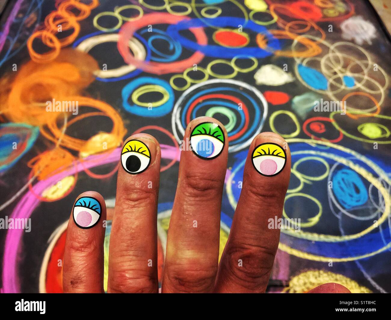 Dark skinned child's fingers with eyes stickers on them in front of bright chalk artwork Stock Photo