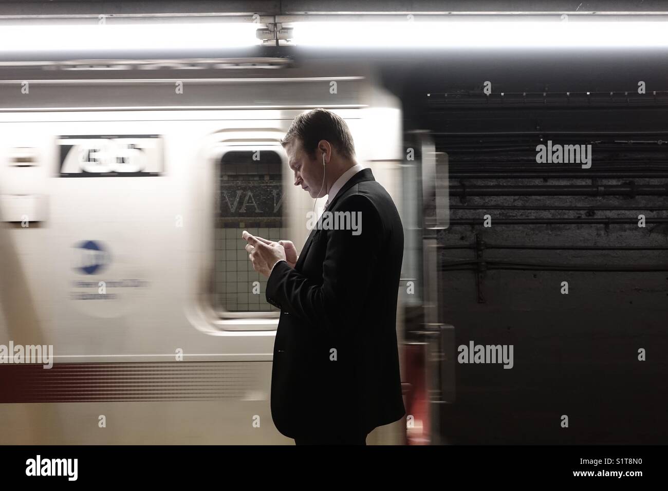 Young adult professional checking in his smartphone while waiting for the MTA subway train - Smartphone Captured Stock Image