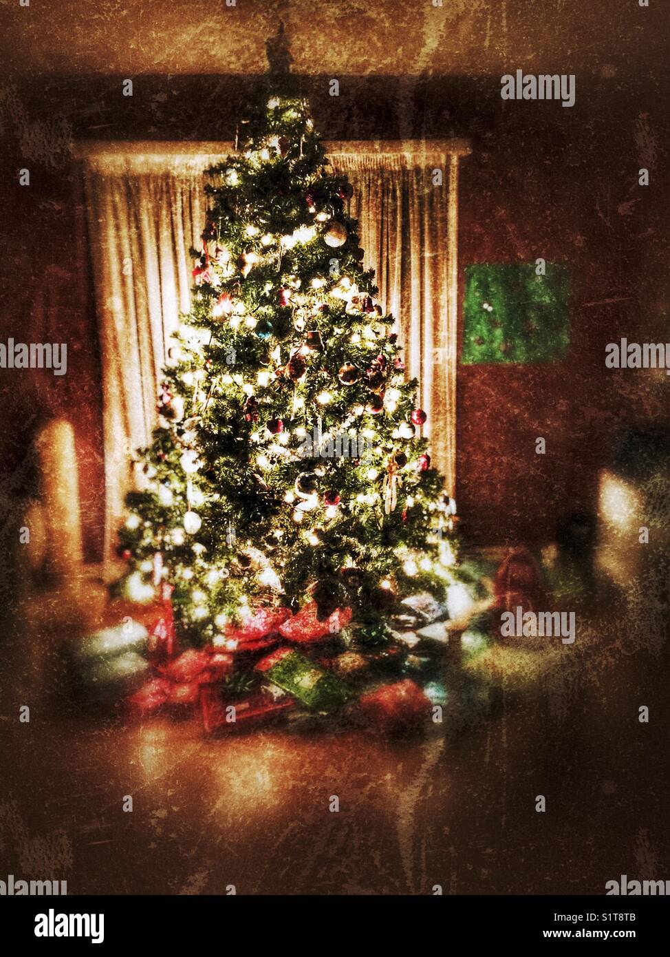 Heavily filtered image of illuminated Christmas tree on Christmas Eve night with presents underneath - Smartphone Captured Stock Image