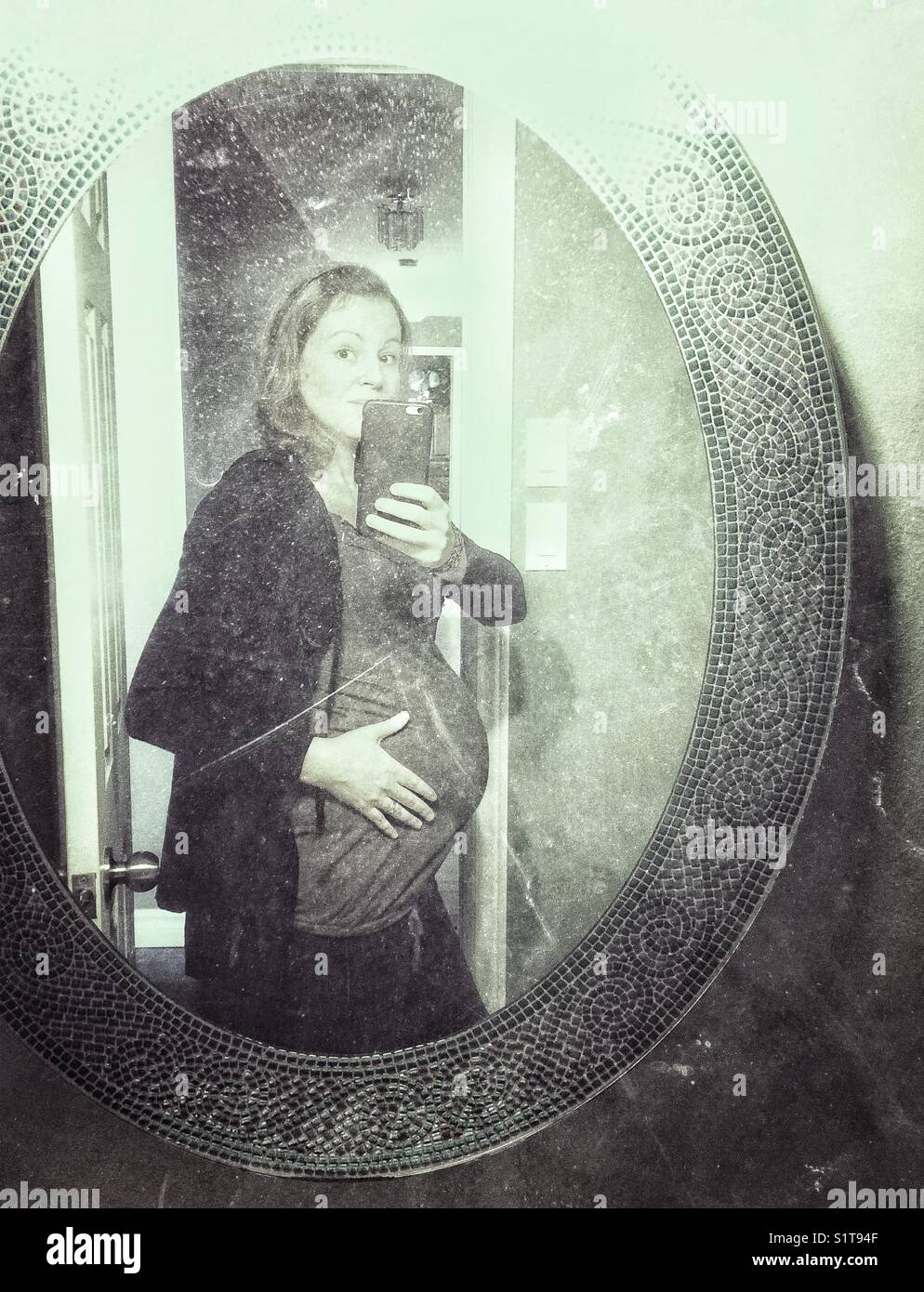 Pregnant woman taking selfie in an oval bathroom mirror Stock Photo