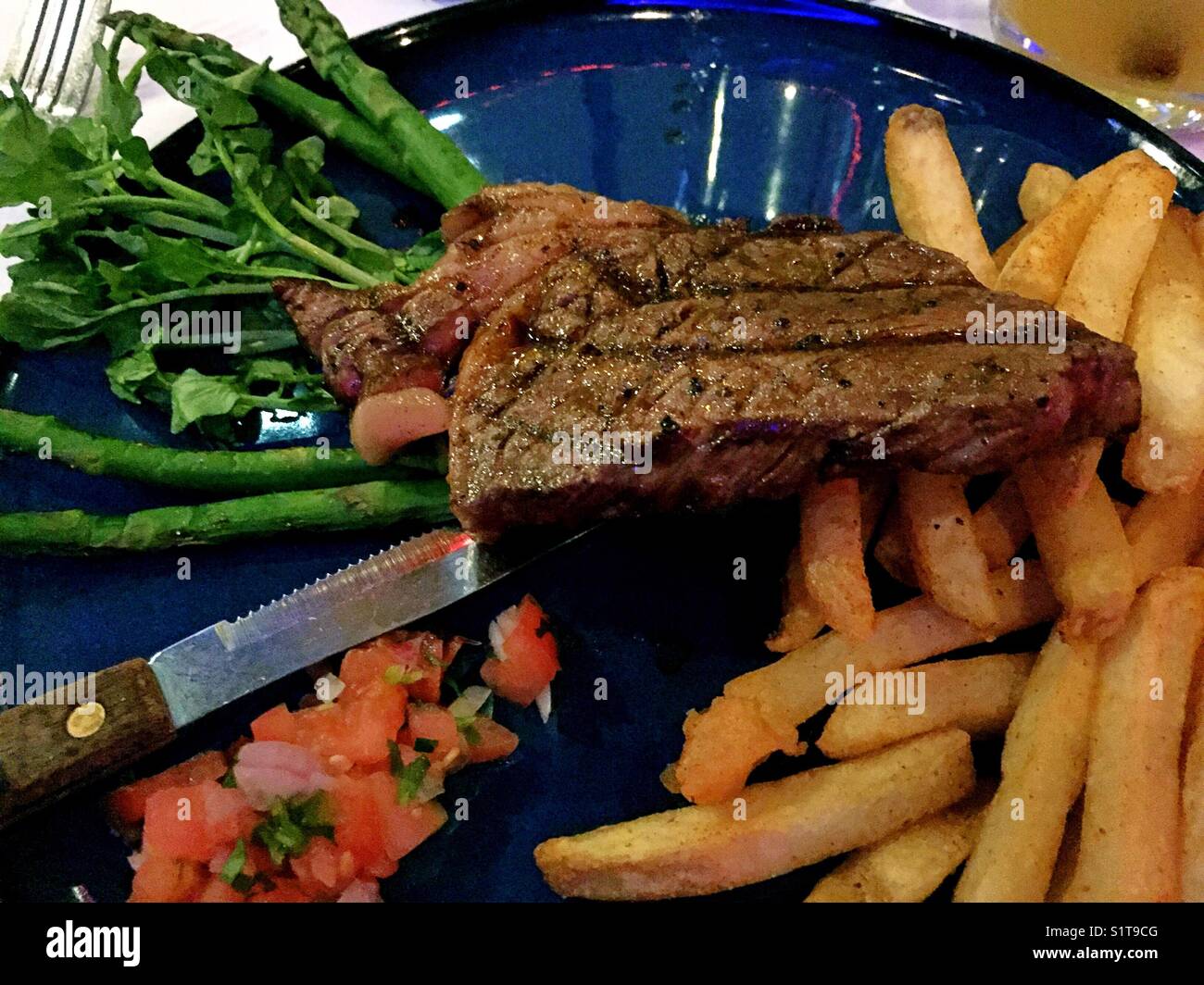 Close-up of grilled ribeye steak served with spicy fries and grilled asparagus - Smartphone Captured Stock Image