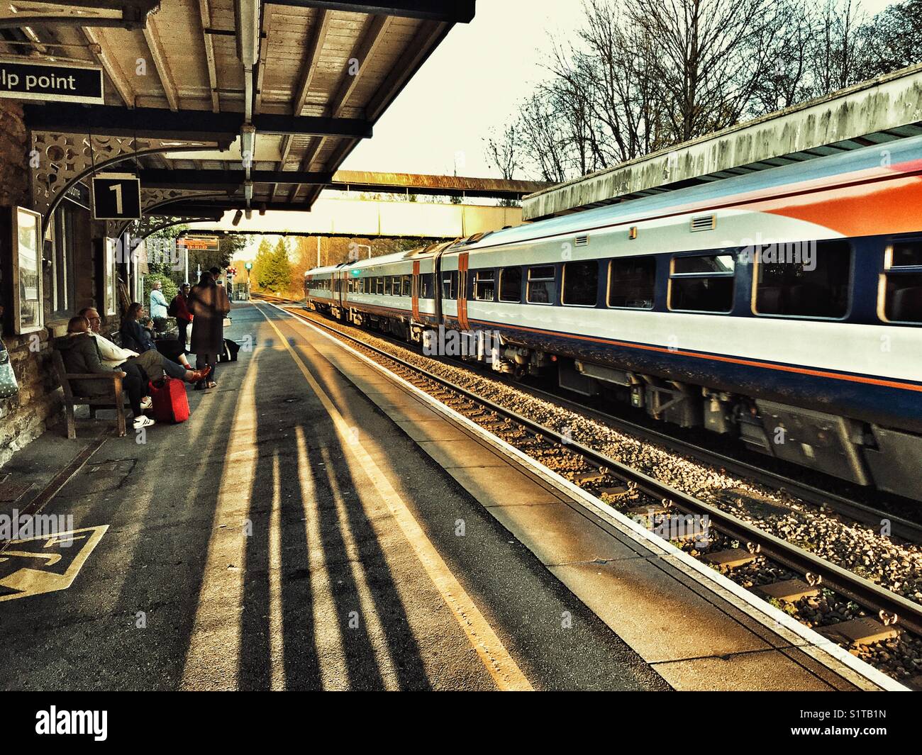 People and shadows on the rail station platform with a train in the station. Sherborne, Dorset, England - Smartphone Captured Stock Image