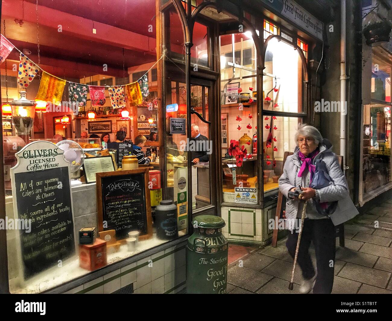 Woman walking past Oliver’s Coffee shop in Cheap Street, on a later winter afternoon. Sherborne, Dorset, England - Smartphone Captured Stock Image