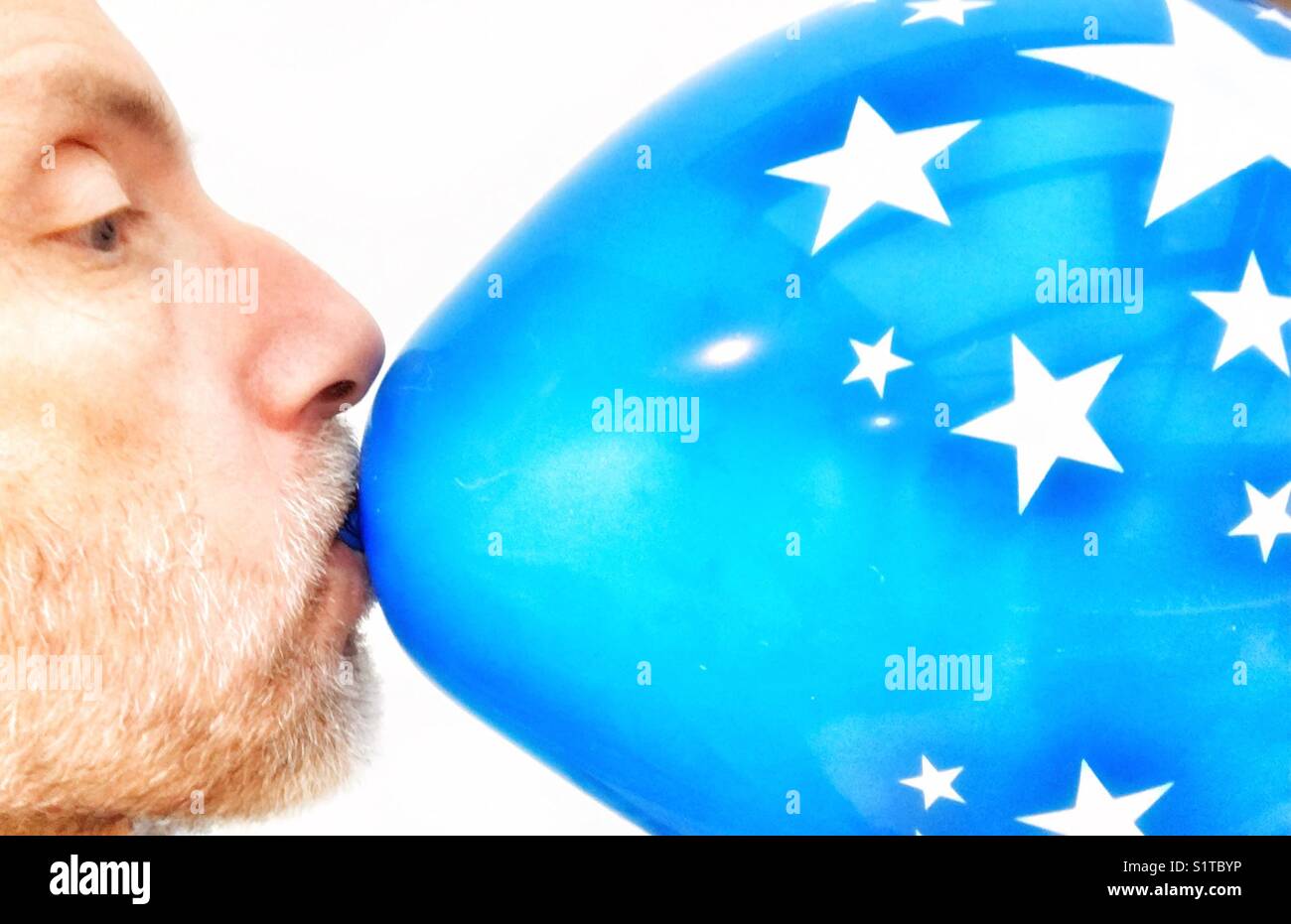 Middle aged man blowing up a blue balloon with star motif Stock Photo