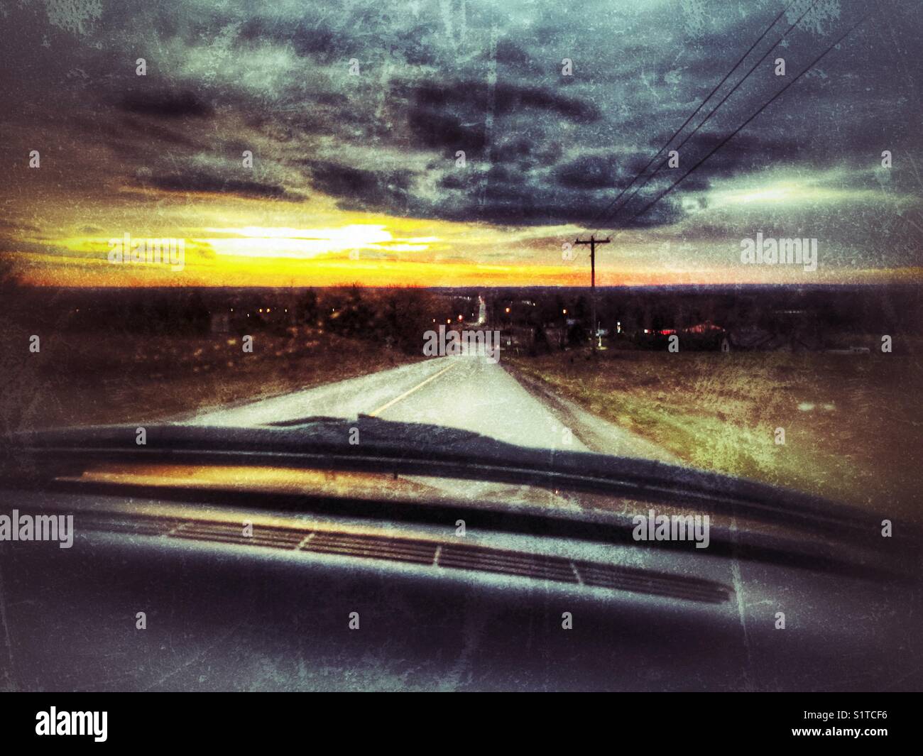 Driving in a truck down an empty road into the bright sunset with dark clouds and hydro wires in view - Smartphone Captured Stock Image
