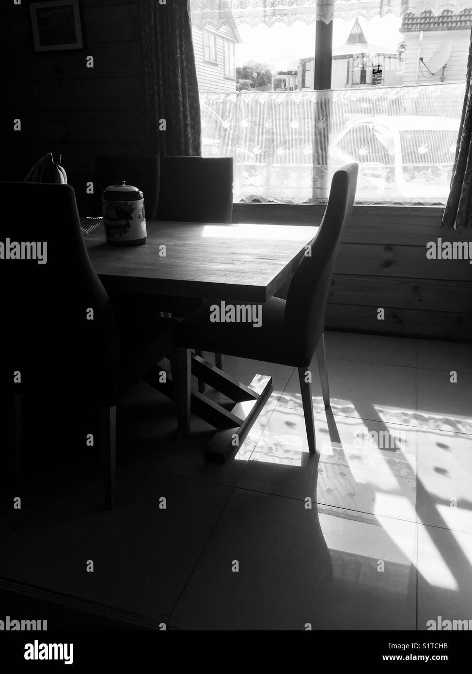 Black and white image of a dining table in the shadows and light of an open window Stock Photo