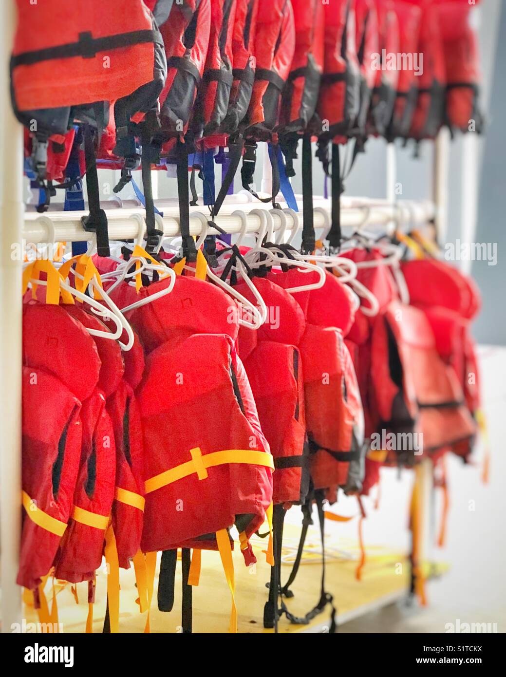 Red life jackets hanging poolside in a community recreation centre Stock Photo