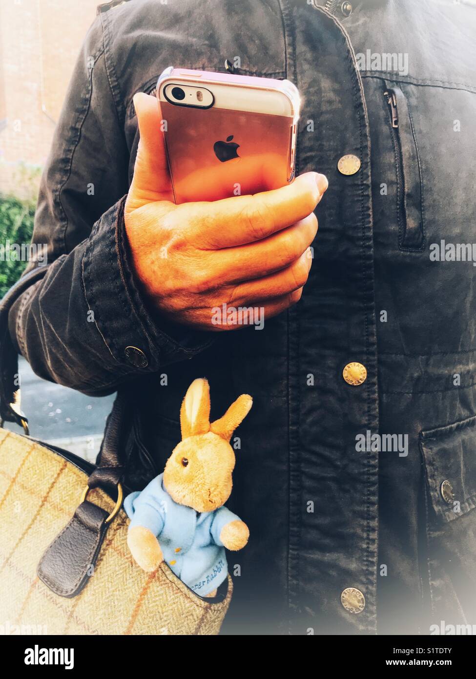 Working mother, using mobile phone and with a toy rabbit sticking out of her handbag. - Smartphone Captured Stock Image