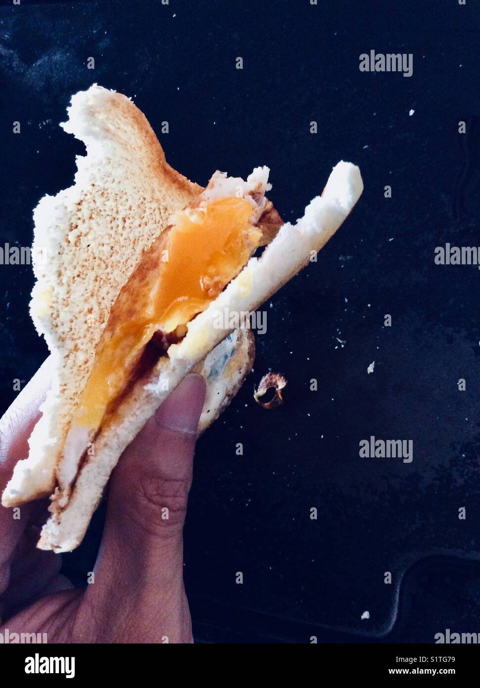 Half fried egg yolk and bitten toasted bread sandwich on black background Stock Photo