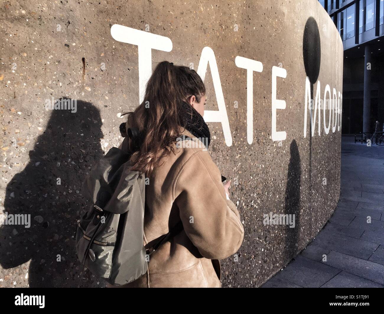 A young woman walks past a Tate Modern sign on a wall outside the gallery in Bankside in London, England on December 1 2017 - Smartphone Captured Stock Image