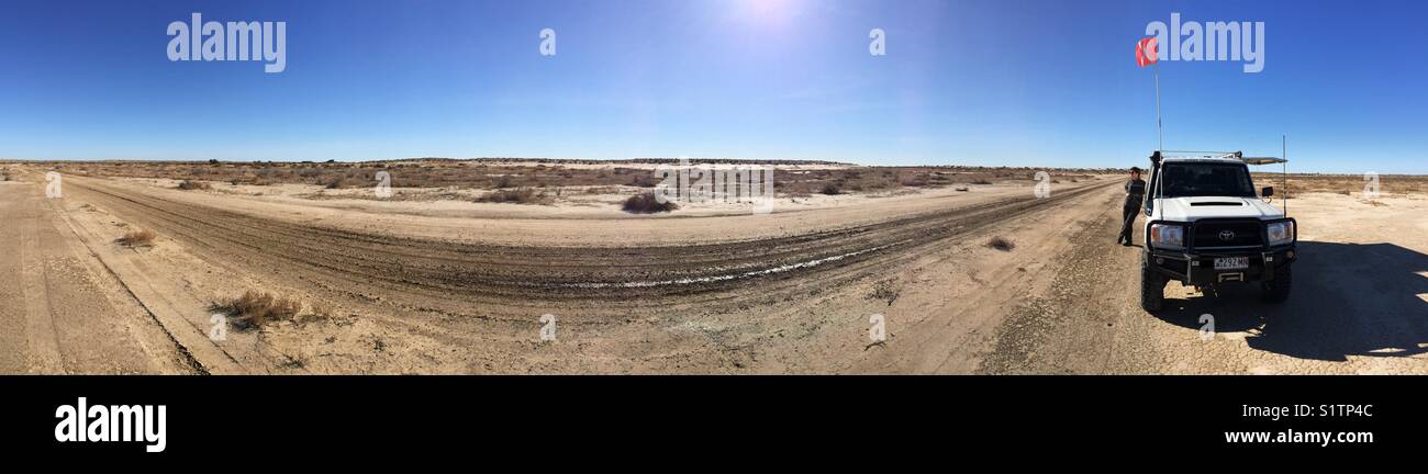180 degrees panorama showing a four wheel drive and sand flag with blue sky and a sun flare in the Australian desert - Smartphone Captured Stock Image