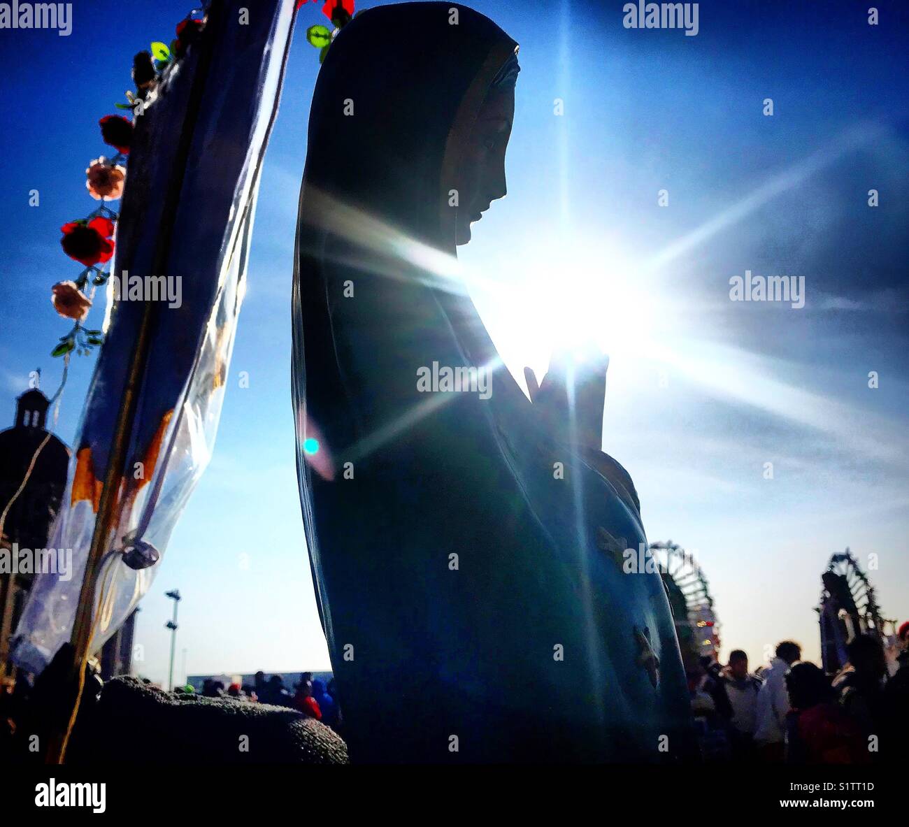 The sun shines in the hands of a sculpture of Our Lady of Guadalupe  during the anual pilgrimage to the Basilica de Nuestra Señora de Guadalupe in Mexico City, Mexico - Smartphone Captured Stock Image