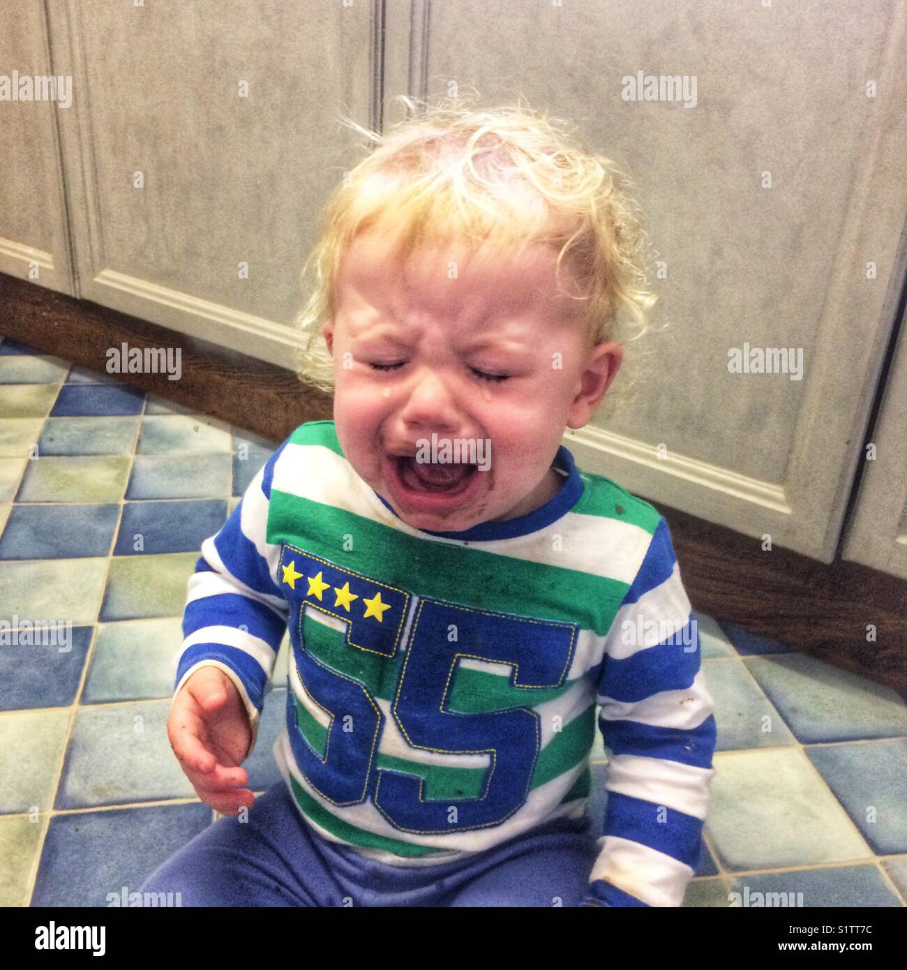 One year old boy with a chocolate covered mouth having a tantrum on the kitchen floor. Stock Photo