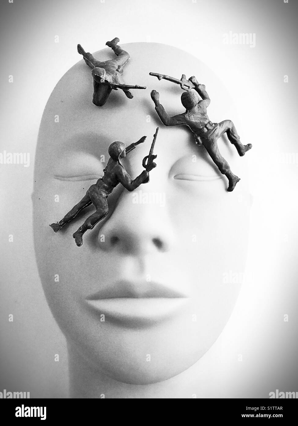 Toy plastic soldiers climbing on a mannequin head. Stock Photo