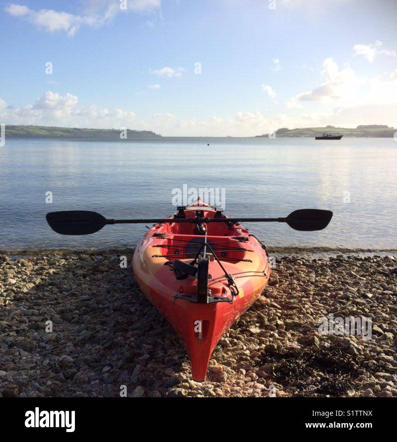 A red sit on Kayak on a beach with a flat sea in the background - Smartphone Captured Stock Image
