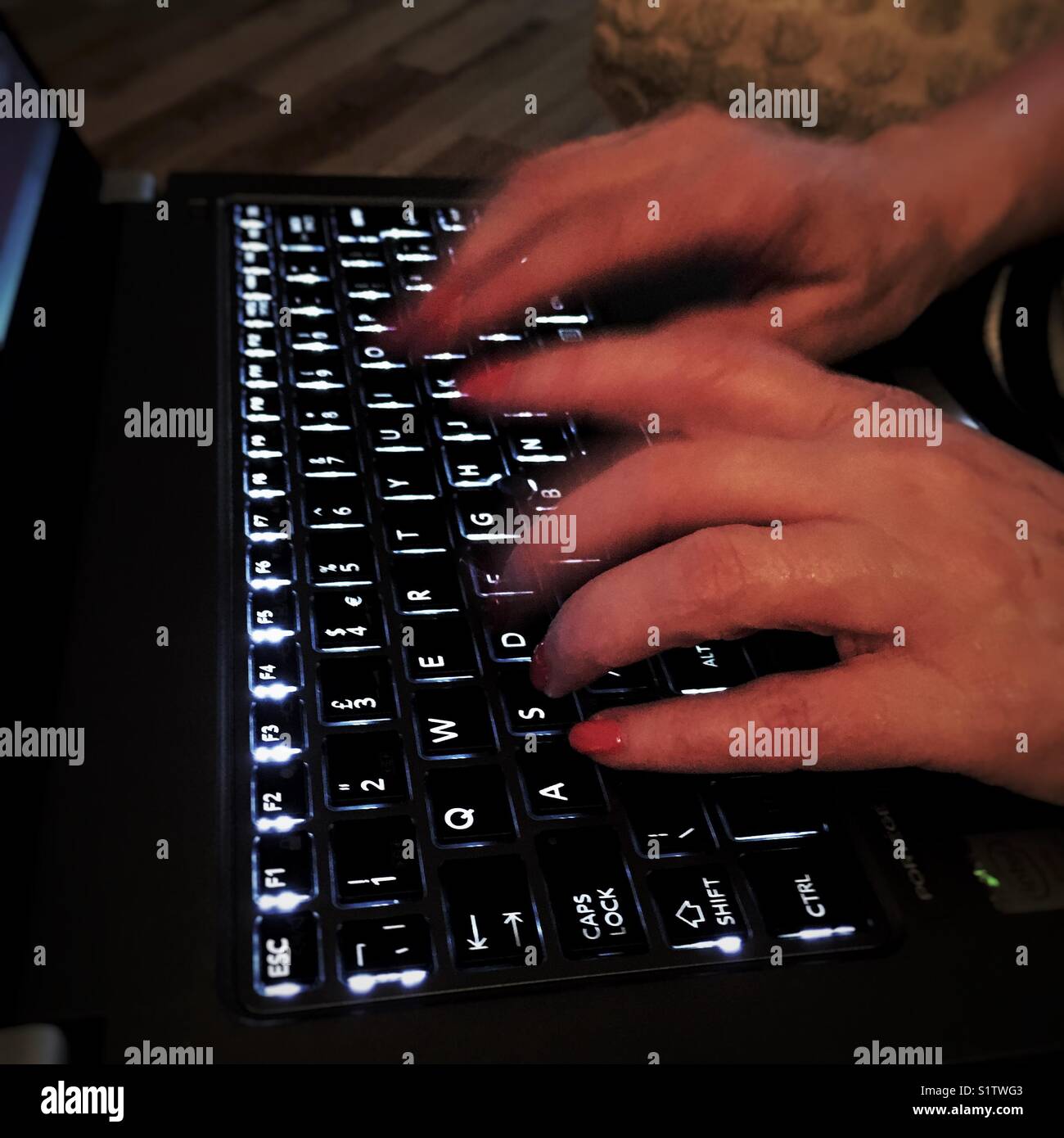 A woman furiously typing away on a backlit QWERTY keyboard of laptop computer, UK - Smartphone Captured Stock Image