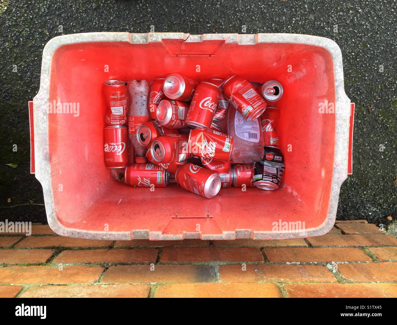 Empty Coca Cola cans in a red recycling container. Builth Wells, Powys, Wales, UK. - Smartphone Captured Stock Image