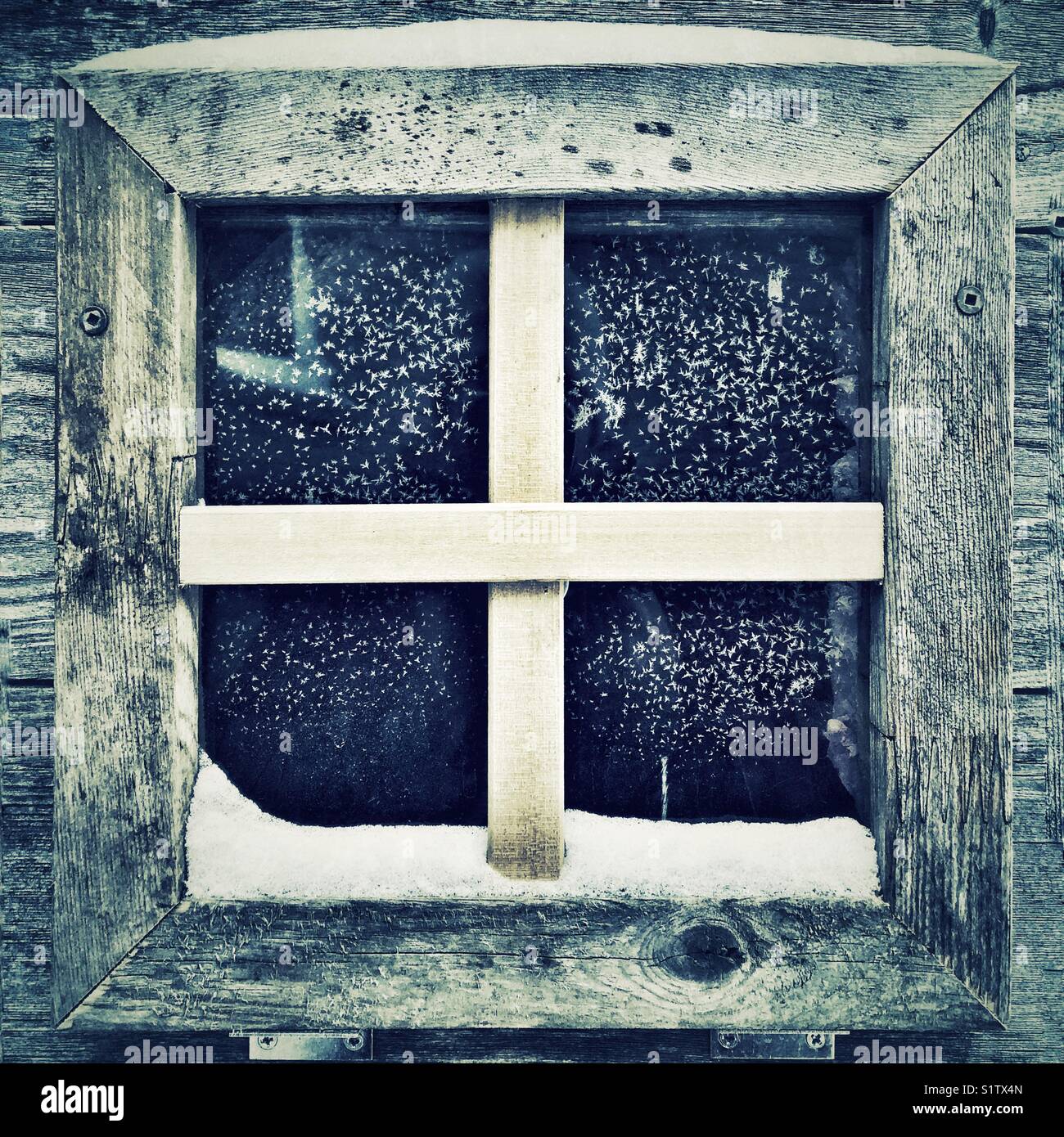 Small square window on a chicken coop with frost covered glass and snow on wooden frame Stock Photo