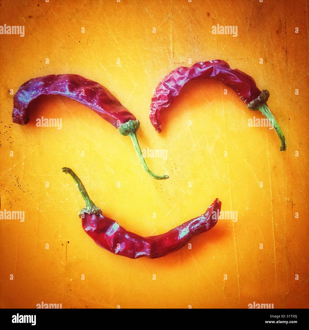 Sun dried red chilli peppers resembling a happy face in an orange cutting board - Smartphone Captured Stock Image