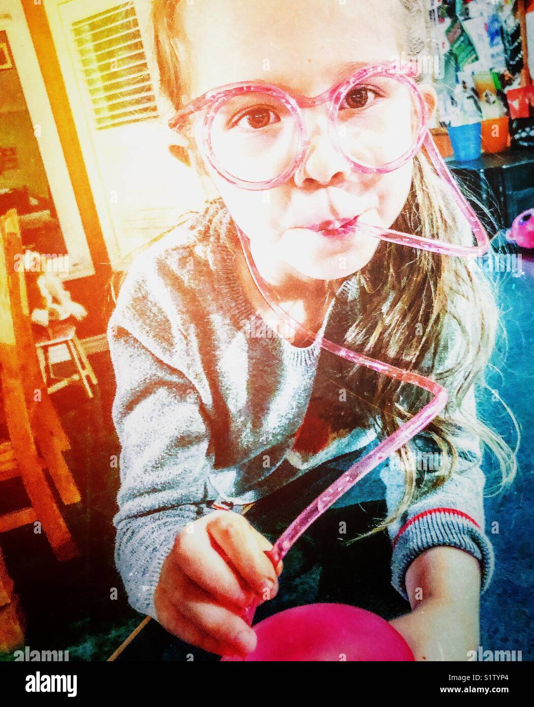 5 year old girl drinking water with a curly, crazy pink straw that runs around face like eyeglasses - Smartphone Captured Stock Image