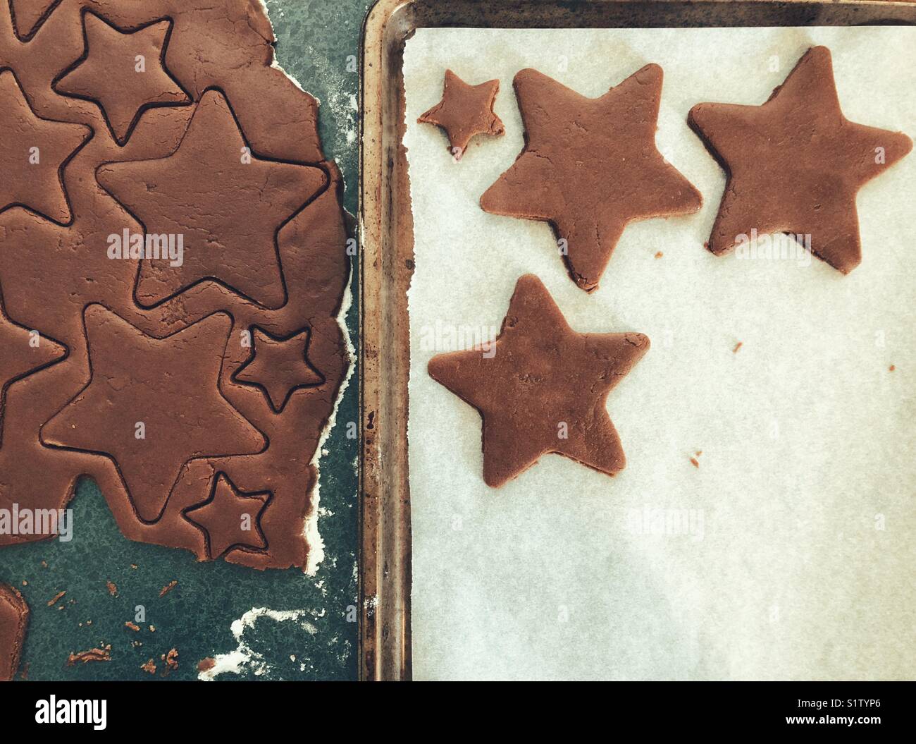 Cutting out star shaped chocolate sugar cookies from dough into pan with parchment paper for Christmas - Smartphone Captured Stock Image